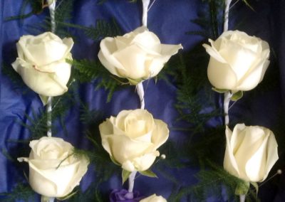 Ten white rose buttonholes rest in on blue satin.